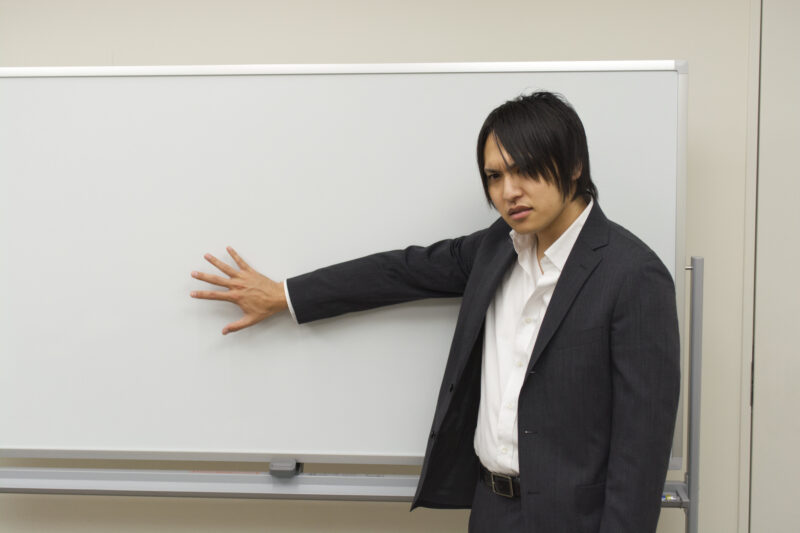 ホワイトボードを指しながら不満げな表情をするビジネスマン