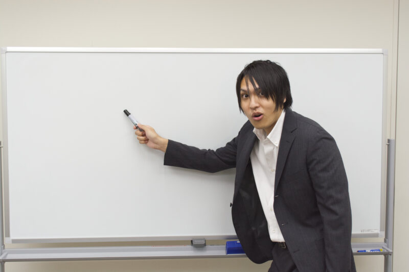 驚いた表情でホワイトボードを指すビジネスマン